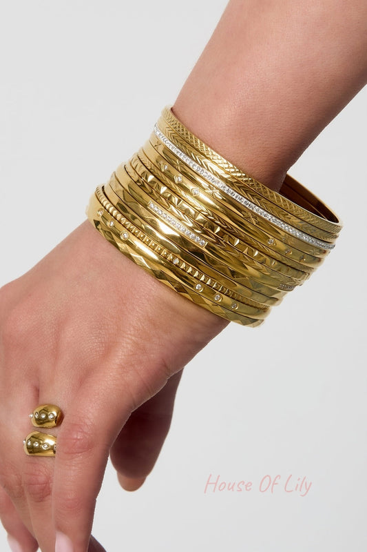 Wrist wearing a stack of 11 gold bangles with varied textures and embedded stones, paired with a gold ring with rhinestones