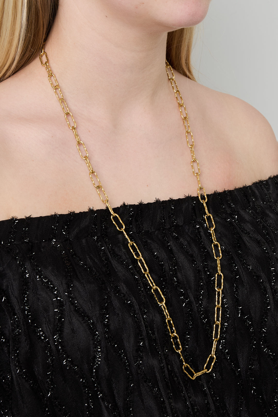 Model showcasing the long gold link chain necklace without pendant, styling a black off-shoulder textured top