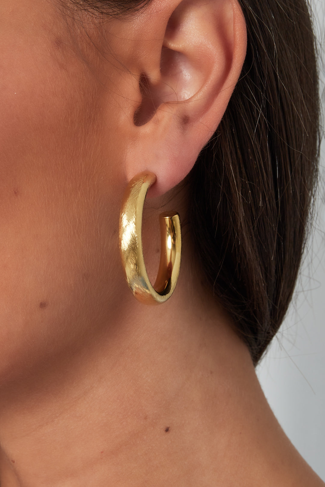 Close-up of a woman wearing chunky gold hoop earring showcasing its texture and size on her ear