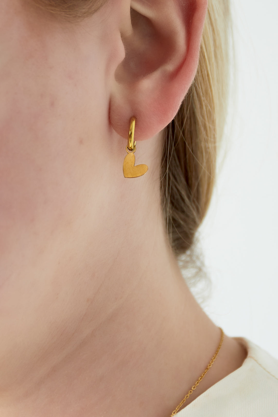 Close-up of woman wearing a gold heart drop earring highlighting delicate design and youthful style