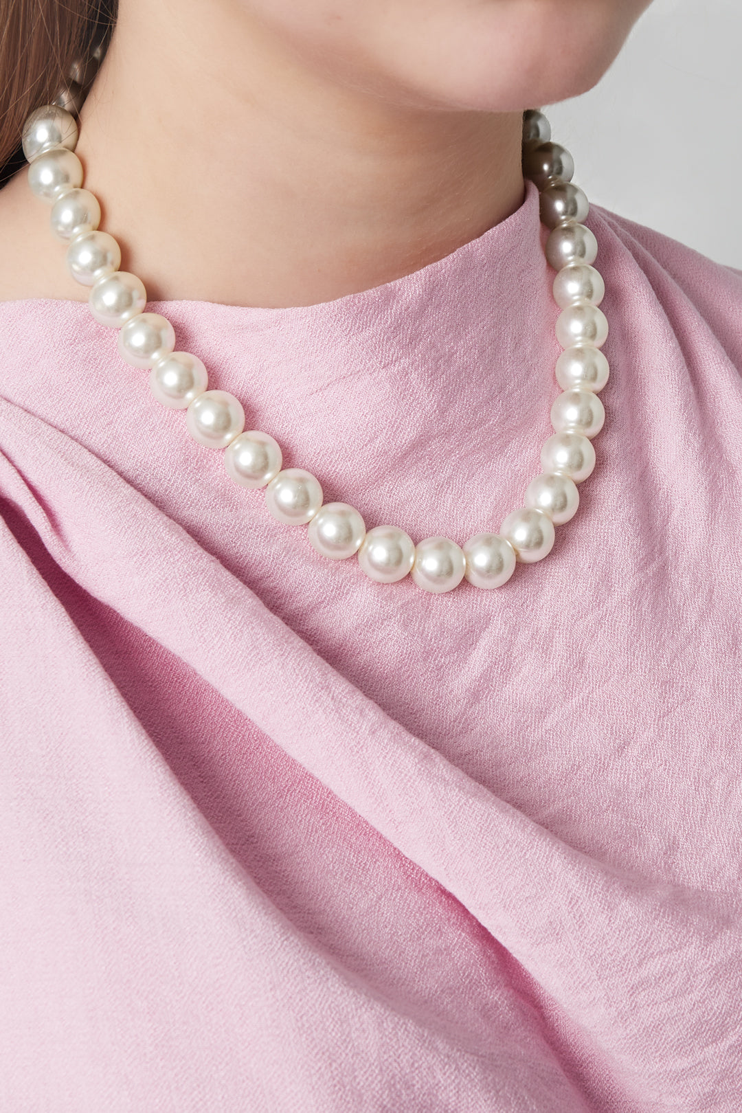 Woman wearing a classic pearl beaded necklace paired with a soft pink blouse, showcasing the necklace’s elegant fit around the neck