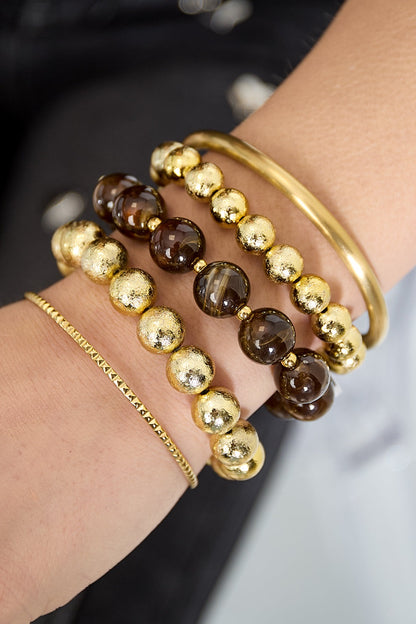 Close-up of wrist with bracelets including dark brown marbled and textured gold bead bracelets styled with gold bangle