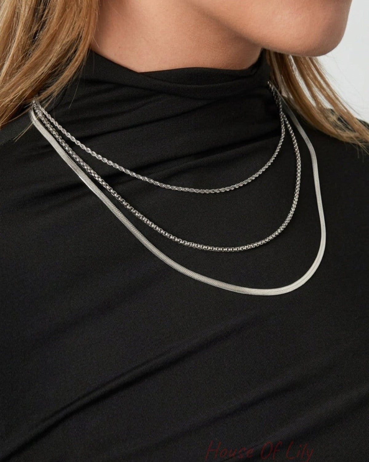 House Of Lily layered silver necklaces on a person wearing a black top.
