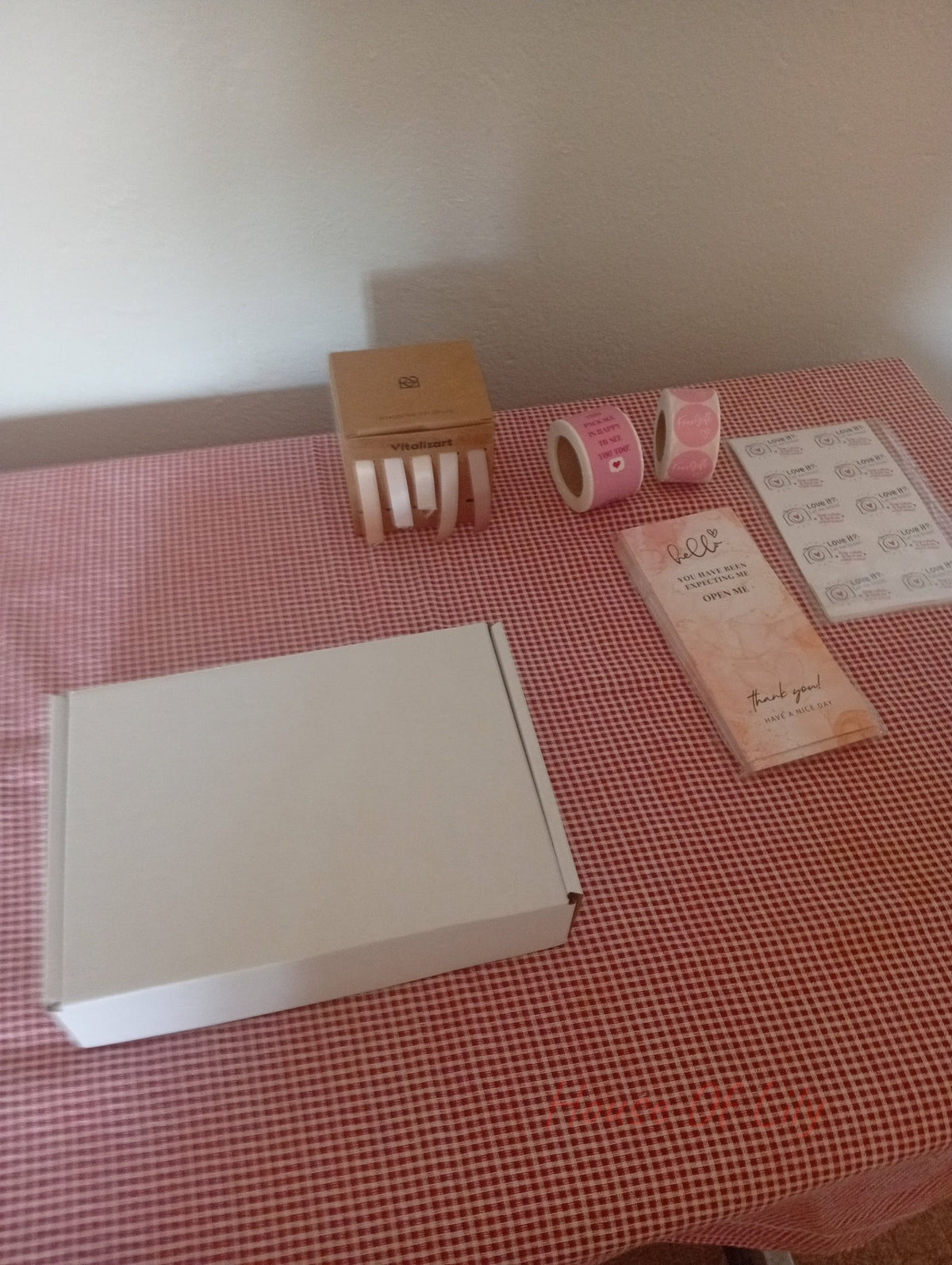 Mystery Box: Launch Edition featuring a white box, stickers, and packaging materials on a red checkered table.