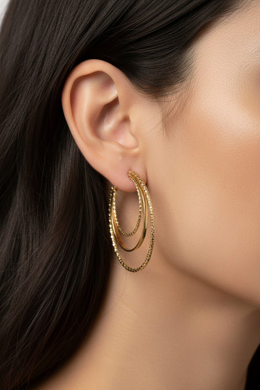Stacked Aura gold hoop earrings featuring textured, beaded surfaces worn on an earlobe.