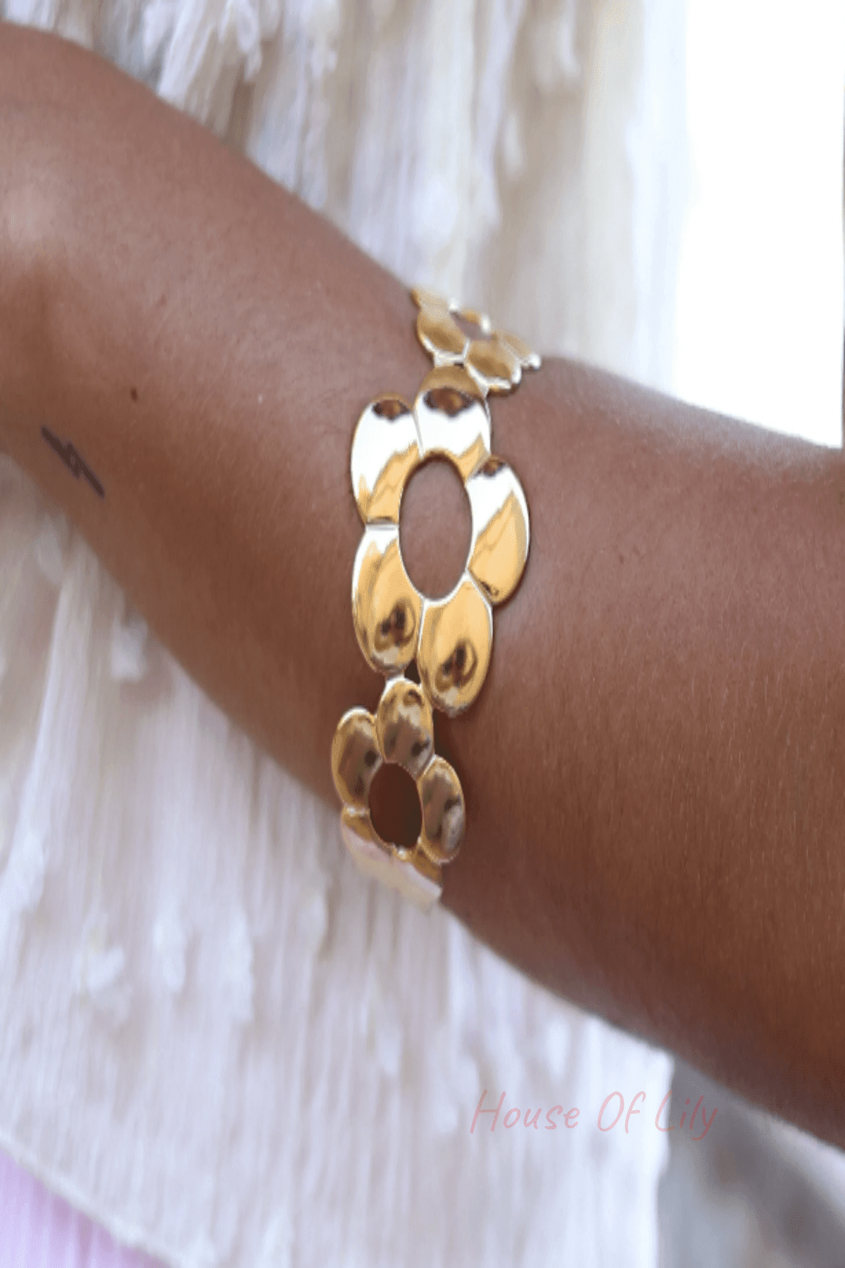 Gold-tone cuff bracelet featuring a series of polished floral cutouts worn on an arm.