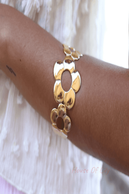 Gold-tone cuff bracelet featuring a series of polished floral cutouts worn on an arm.