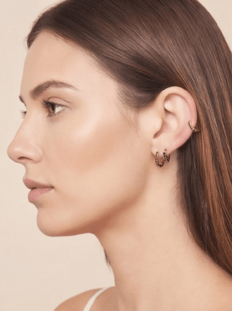 Model wearing gold small hoop earrings and a matching ear cuff, each accented with delicate black crystals.