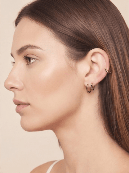 Model wearing gold small hoop earrings and a matching ear cuff, each accented with delicate black crystals.