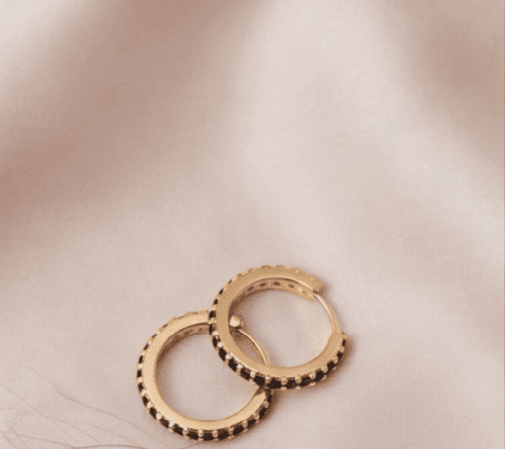 Crystal Sparkle Hoops: Gold hoop earrings featuring a row of small, sparkling black stones on a soft silk background.