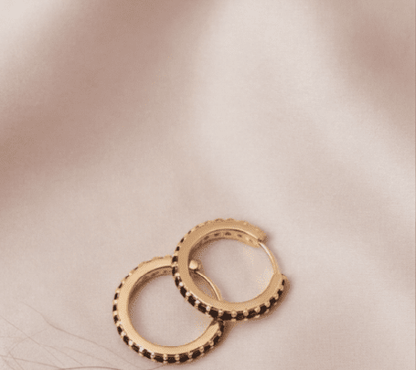 Crystal Sparkle Hoops: Gold hoop earrings featuring a row of small, sparkling black stones on a soft silk background.