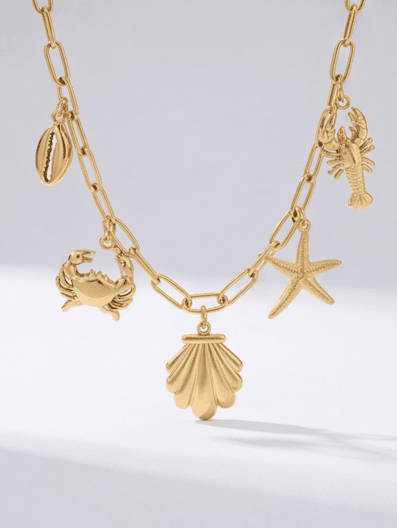 Gold chain bracelet featuring seaside-themed charms including a scallop shell, starfish, crab, lobster, and cowrie shell.
