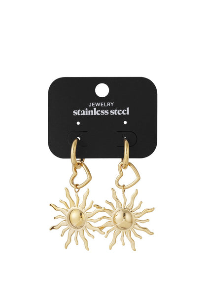 Gold stainless steel drop earrings featuring heart charms and sunburst pendants on a black display card.