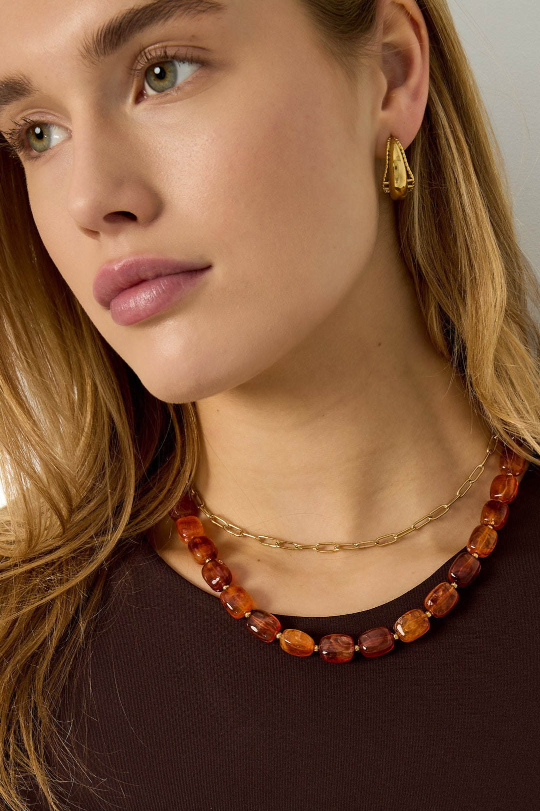 Woman wearing chunky multicolor (blue, green, red, amber, brown) acrylic beaded necklace layered with gold chain and gold earrings