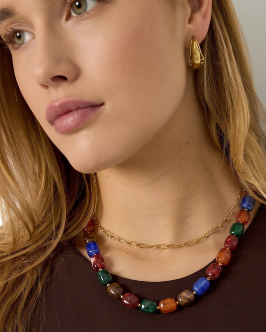 A woman wears a colorful rectangular beaded necklace alongside a simple gold chain.