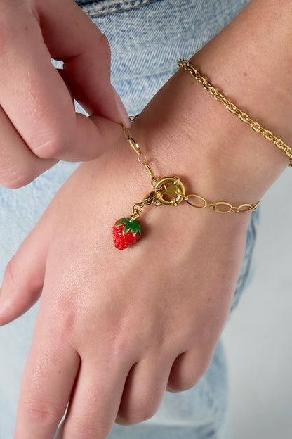 Close-up of wrist wearing gold-tone chain bracelet with strawberry charm and additional chain bracelet over denim fabric