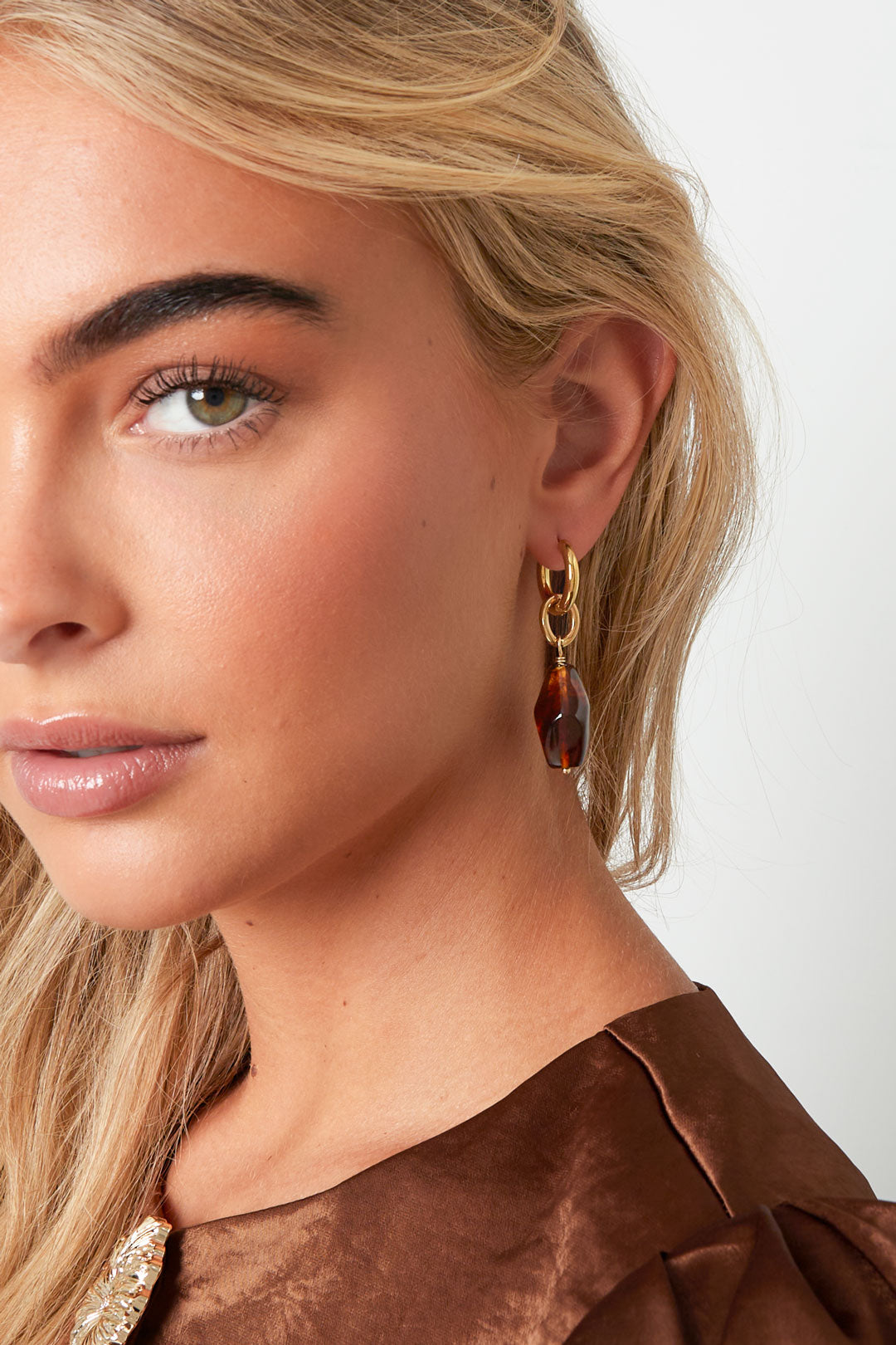 Close-up of woman wearing gold hoop drop earrings with coffee brown irregular-shaped acrylic charms, paired with brown satin top