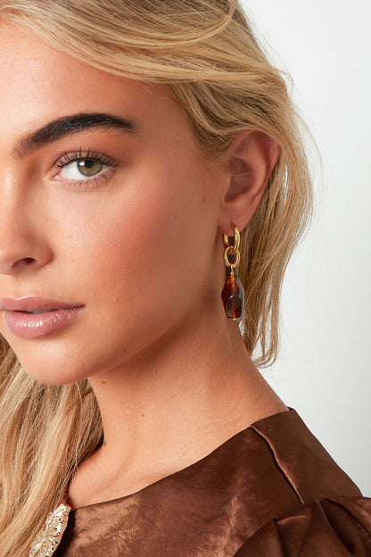 Close-up of woman wearing gold hoop drop earrings with coffee brown irregular-shaped acrylic charms, paired with brown satin top