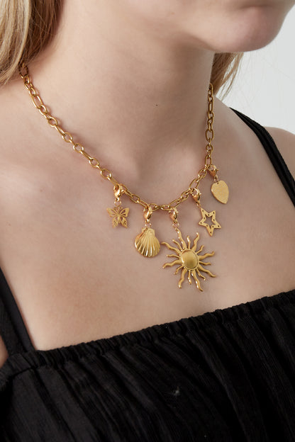 Close-up of a woman wearing gold charm pendant necklace featuring sun, star, heart, butterfly, and seashell charms over black top