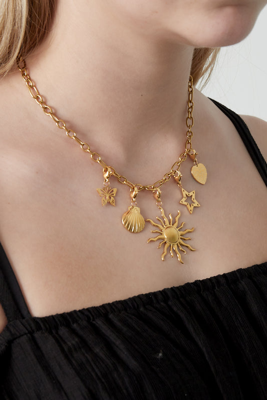 Close-up of a woman wearing gold charm pendant necklace featuring sun, star, heart, butterfly, and seashell charms over black top