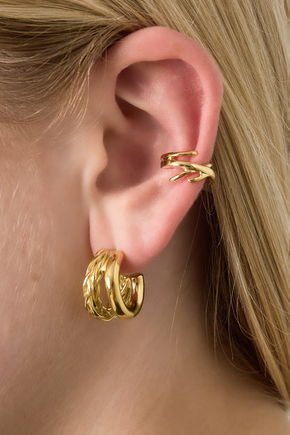 Close-up of ear wearing gold twisted wire ear cuff with additional gold hoops