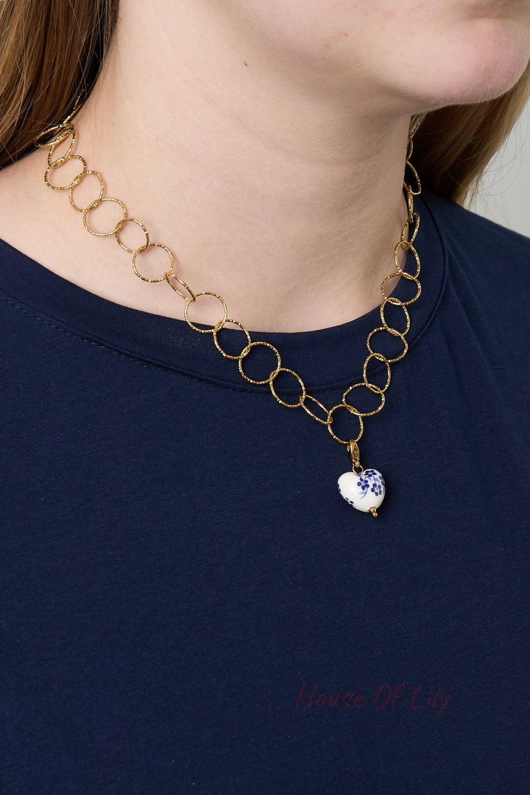 Model wearing gold loop chain necklace featuring a detachable heart-shaped charm with blue floral design