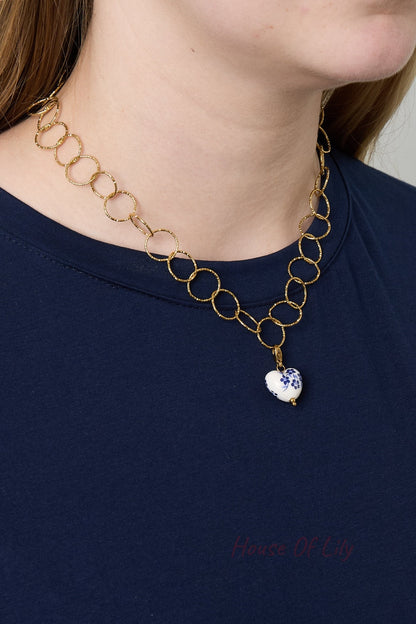Model wearing gold loop chain necklace featuring a detachable heart-shaped charm with blue floral design