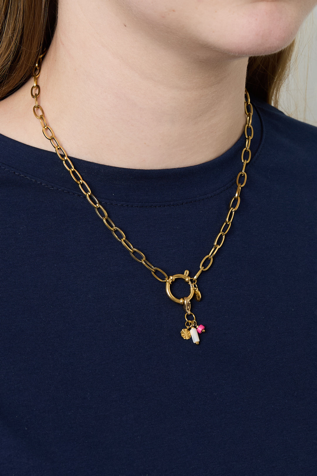 Model wearing gold link chain necklace with toggle clasp and small charms over navy blue top
