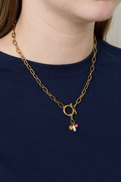Model wearing gold link chain necklace with toggle clasp and small charms over navy blue top