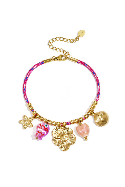 Pink rope charm bracelet with gold beads and assorted charms including a flower, fish, heart, and shell, shown on white background.