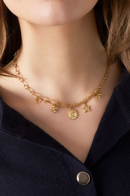 Model wearing the gold charm necklace resting on collarbone with dark top