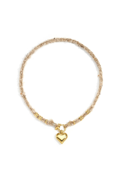 Gold heart pendant necklace with beige textured wool rope chain and gold rings laid flat on white background