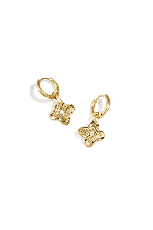 Close-up of gold floral drop earrings with zircon center on white background