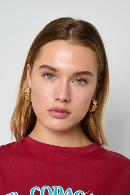 Model wearing Gilt Heart Loops: gold hoop earrings featuring a linked chain of small heart-shaped charms.