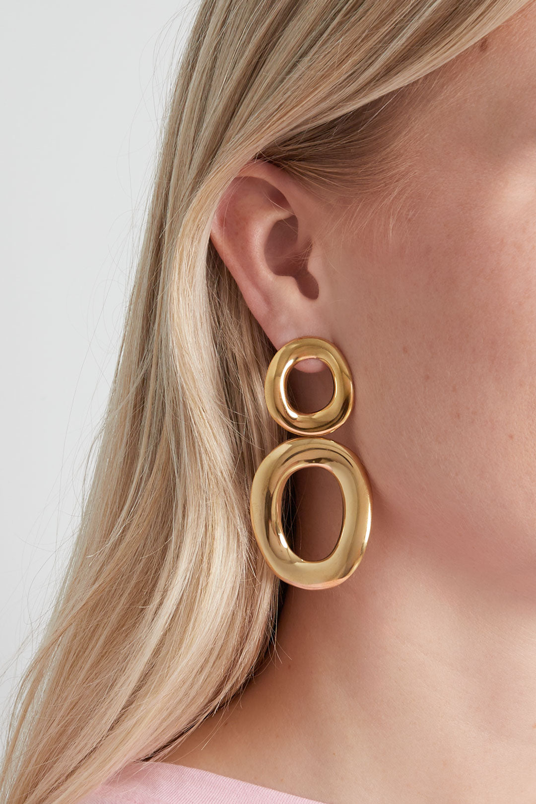 Close-up of a woman wearing shiny gold twist oval drop earrings, showcasing the soft, polished design