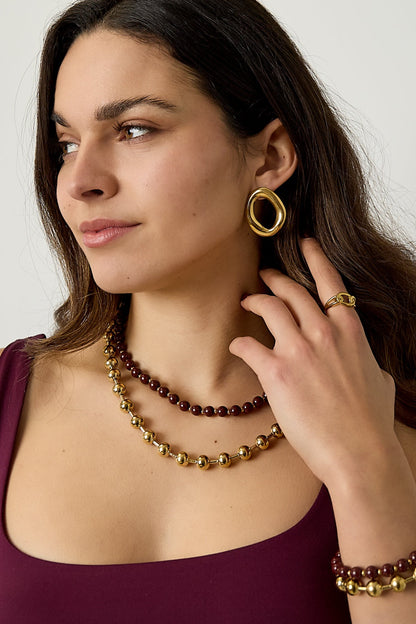 Woman wearing layered bead necklace set with gold hoop earrings and matching ring, showcasing minimal youthful look in dark top