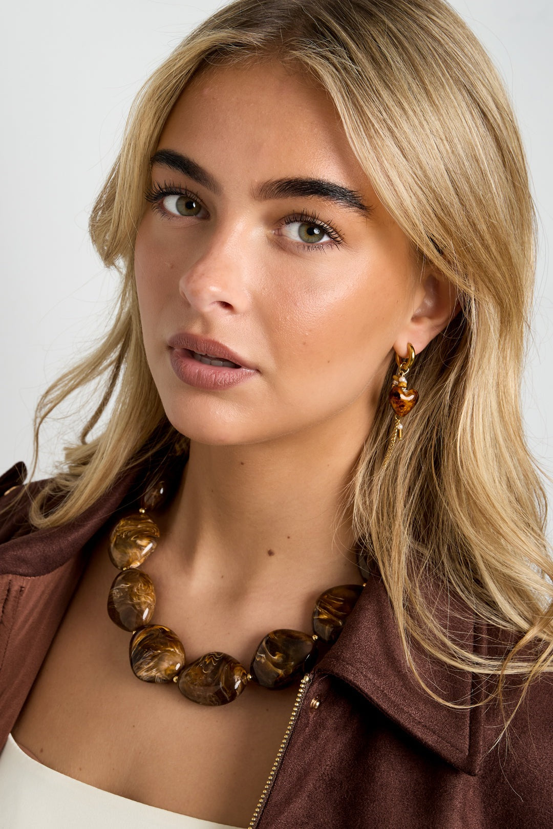 Model wearing chunky brown acrylic beaded necklace paired with matching earrings and brown jacket