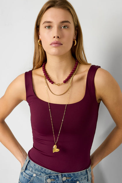 Close-up of model showing navy blue resin bead necklace with gold clasp and layered gold chain necklaces