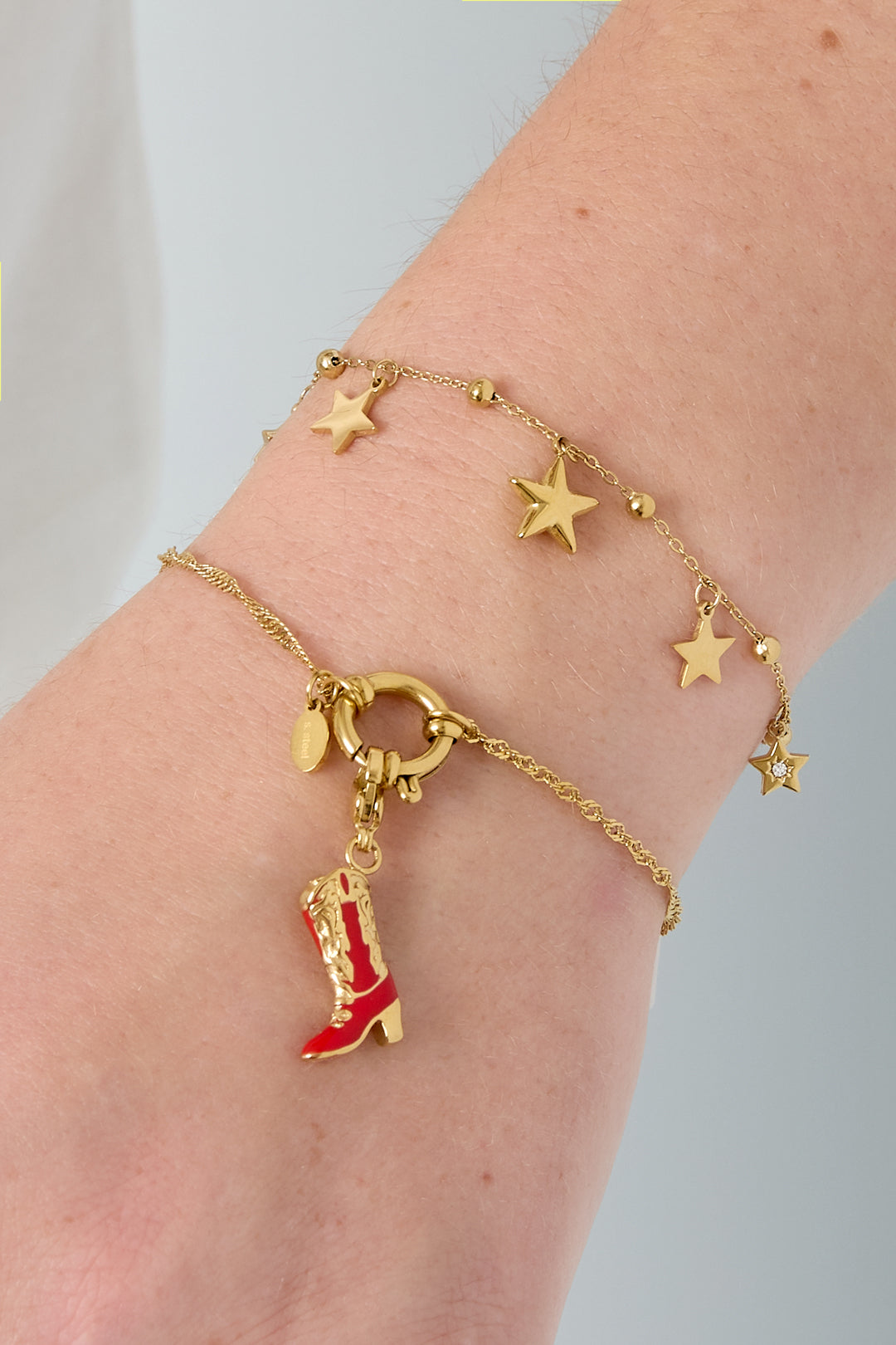Close-up of a wrist wearing a gold star charm bracelet paired with a colorful boot charm bracelet