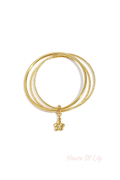 Set of two gold-tone bangles with a hanging flower charm on a white background