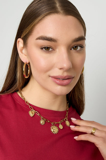 Woman wearing gold sun and heart charm necklace with matching gold hoop earrings and red top