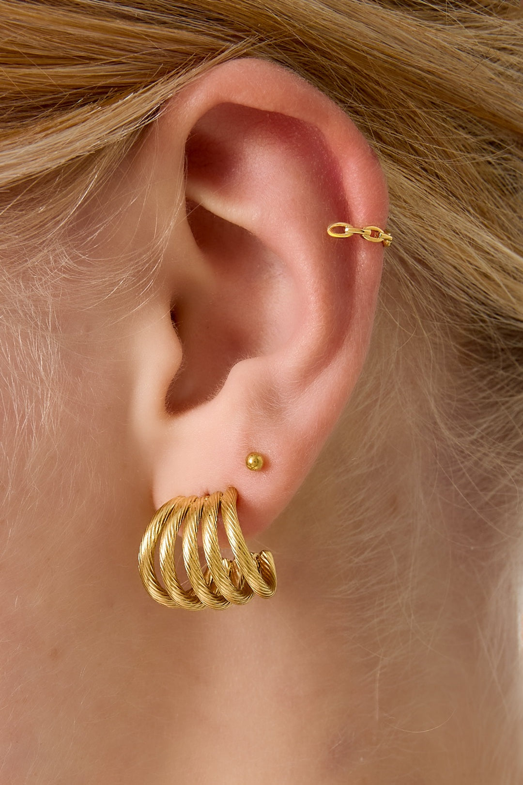 Close-up of woman’s ear wearing gold chain link ear cuff paired with ridged gold hoop earring and small stud