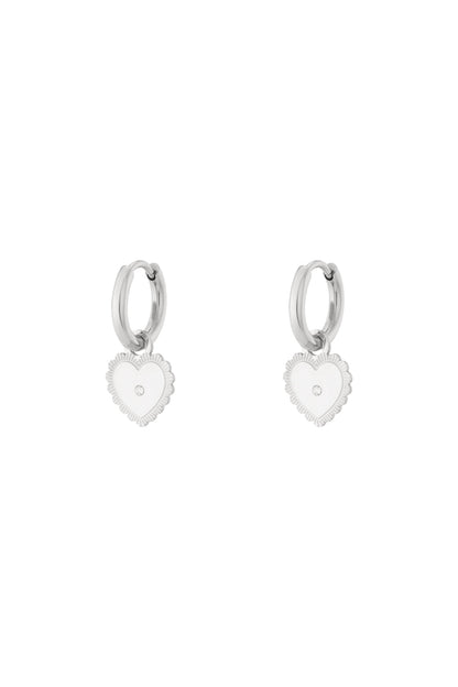 Silver hoop earrings with dangling heart charm featuring central rhinestone on white background