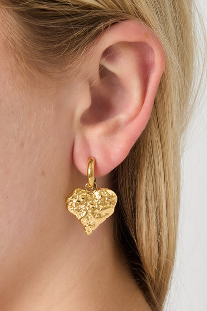 Detailed view of gold textured heart hoop earring worn on ear with smooth hoop and hammered heart charm