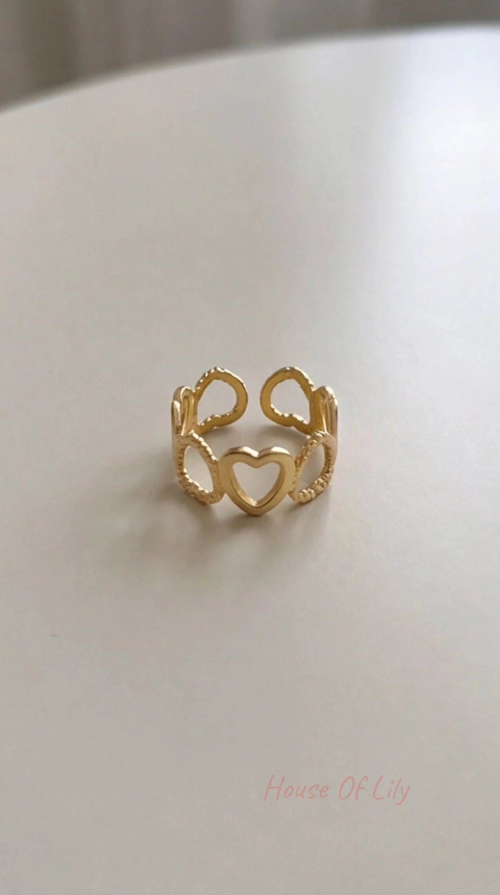 Gold-tone Heart Link open ring with a series of interconnected heart shapes, displayed on a light surface.