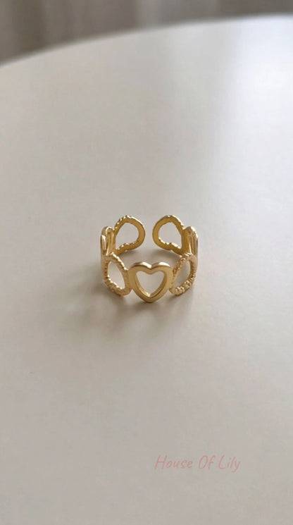 Gold-tone Heart Link open ring with a series of interconnected heart shapes, displayed on a light surface.