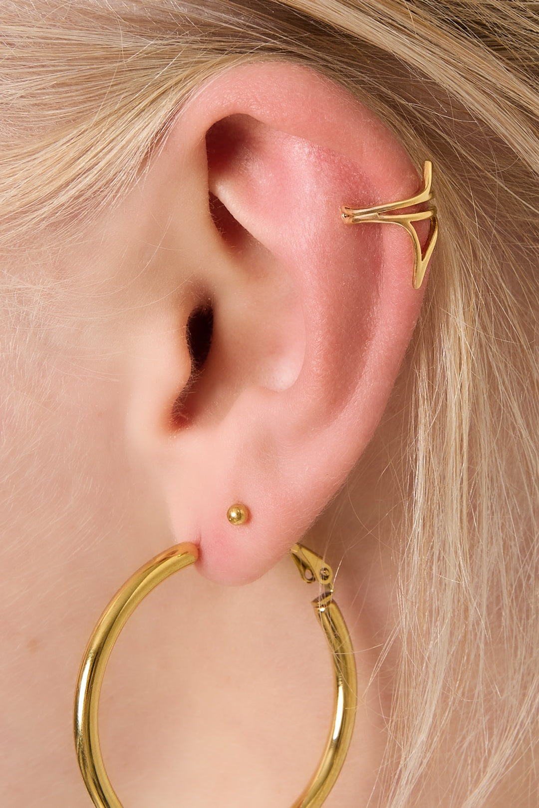 Close-up of woman's ear wearing gold geometric ear cuff with large gold hoop earring and small ball stud