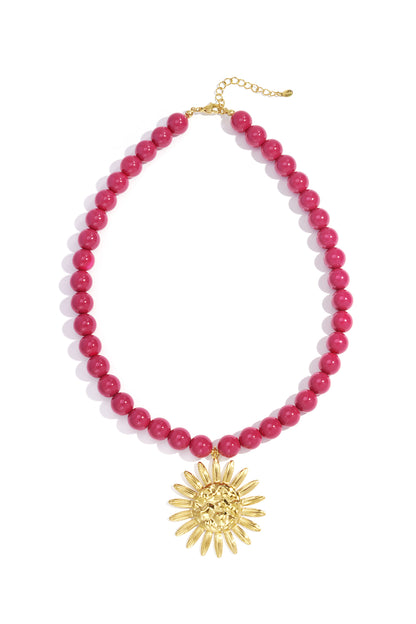 Berry pink beaded necklace with gold sun pendant laid flat on white background showing full necklace shape
