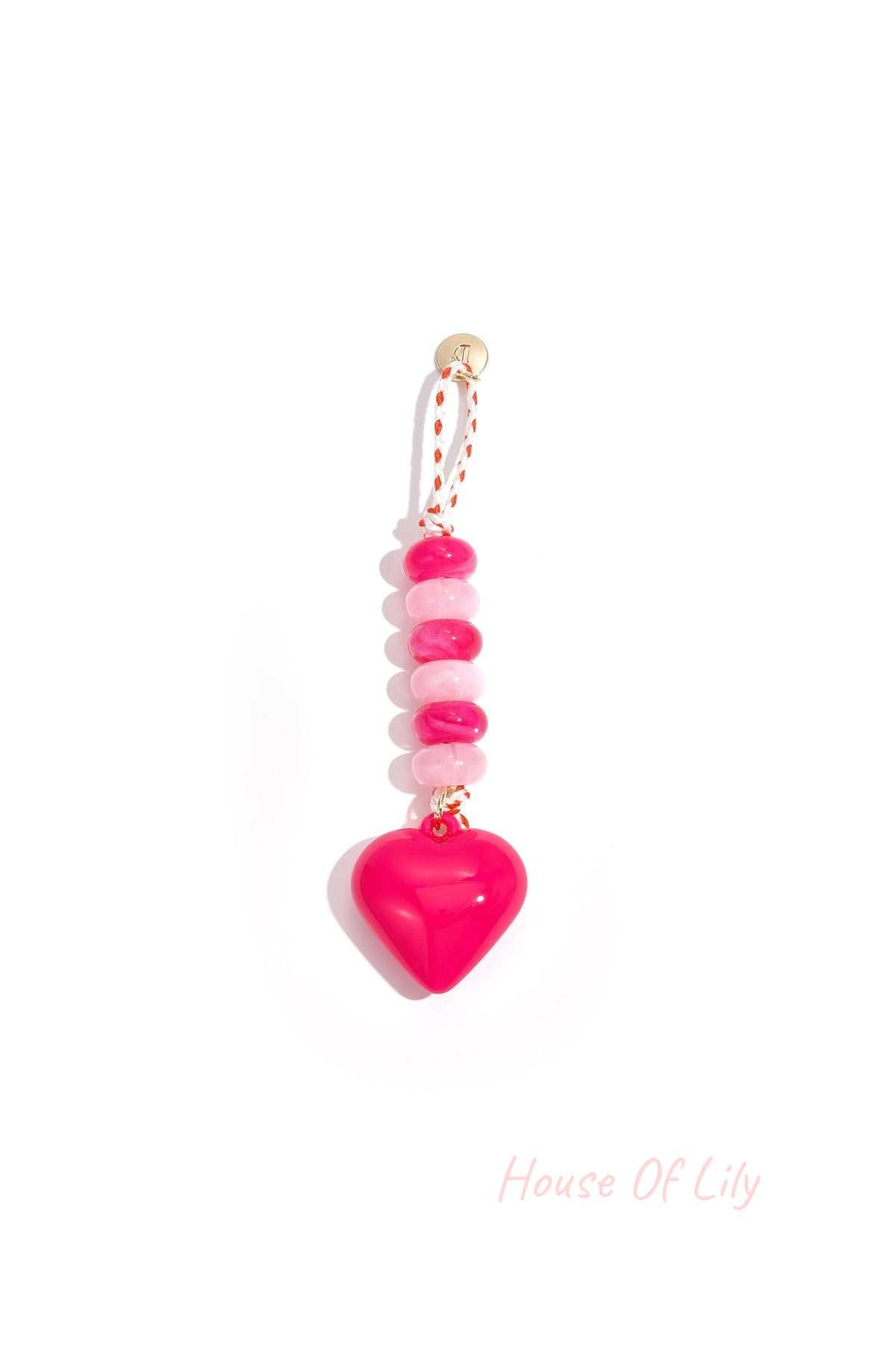 Bright pink heart-shaped acrylic bag charm with alternating light and dark pink beads on a braided pink and white loop with gold accent.