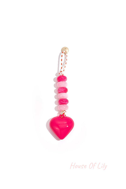 Bright pink heart-shaped acrylic bag charm with alternating light and dark pink beads on a braided pink and white loop with gold accent.